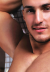 shirtless man gazing at viewer with his arm raised over his head